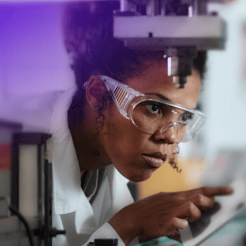 Tecnica di laboratorio con occhiali protettivi durante un controllo qualità al microscopio