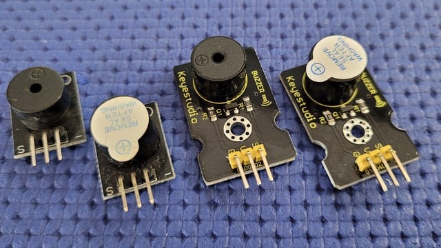 Alcuni buzzer sciolti e montati su moduli, appoggiati su un piano blu